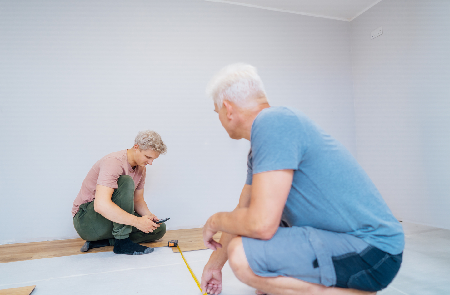 Two men measuring and planning a home renovation using a tape measure, illustrating the precision required when planning handicap bathroom layout dimensions