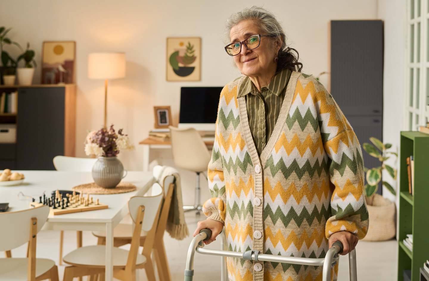 Older woman using a metal walker for fall prevention support while standing in a bright home
