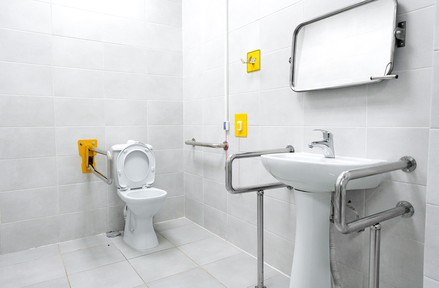 Accessible bathroom with stainless steel grab bars, folding armrest, and emergency call panels installed as part of a planned home fall prevention layout