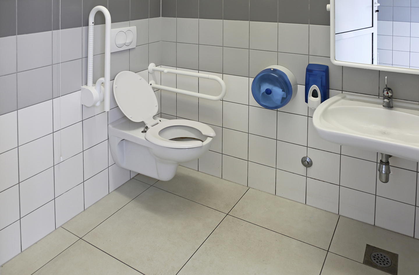 A modern accessible restroom corner with a wall-mounted toilet and both vertical and horizontal grab bars installed on white tiled walls