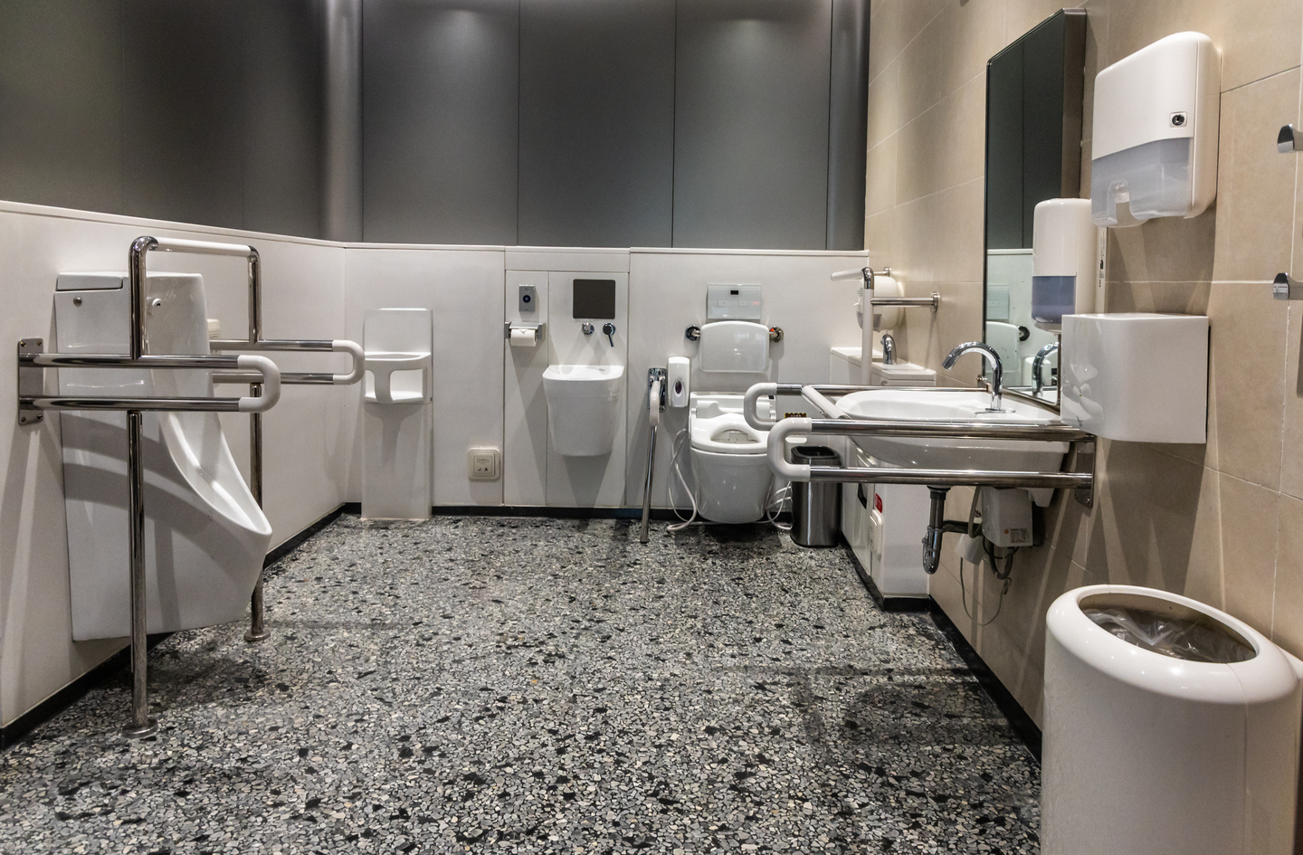 A modern accessible restroom showing wall-mounted grab bars beside a toilet and urinal, key accessible bathroom features for layout planning