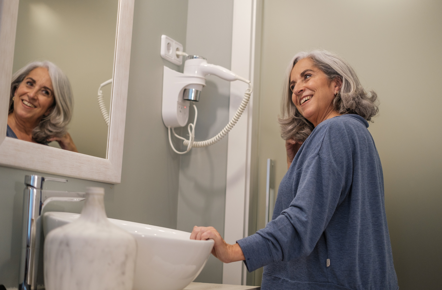 A senior woman using a bathroom sink in a bright, well-lit accessible bathroom - demonstrating daily fixture use