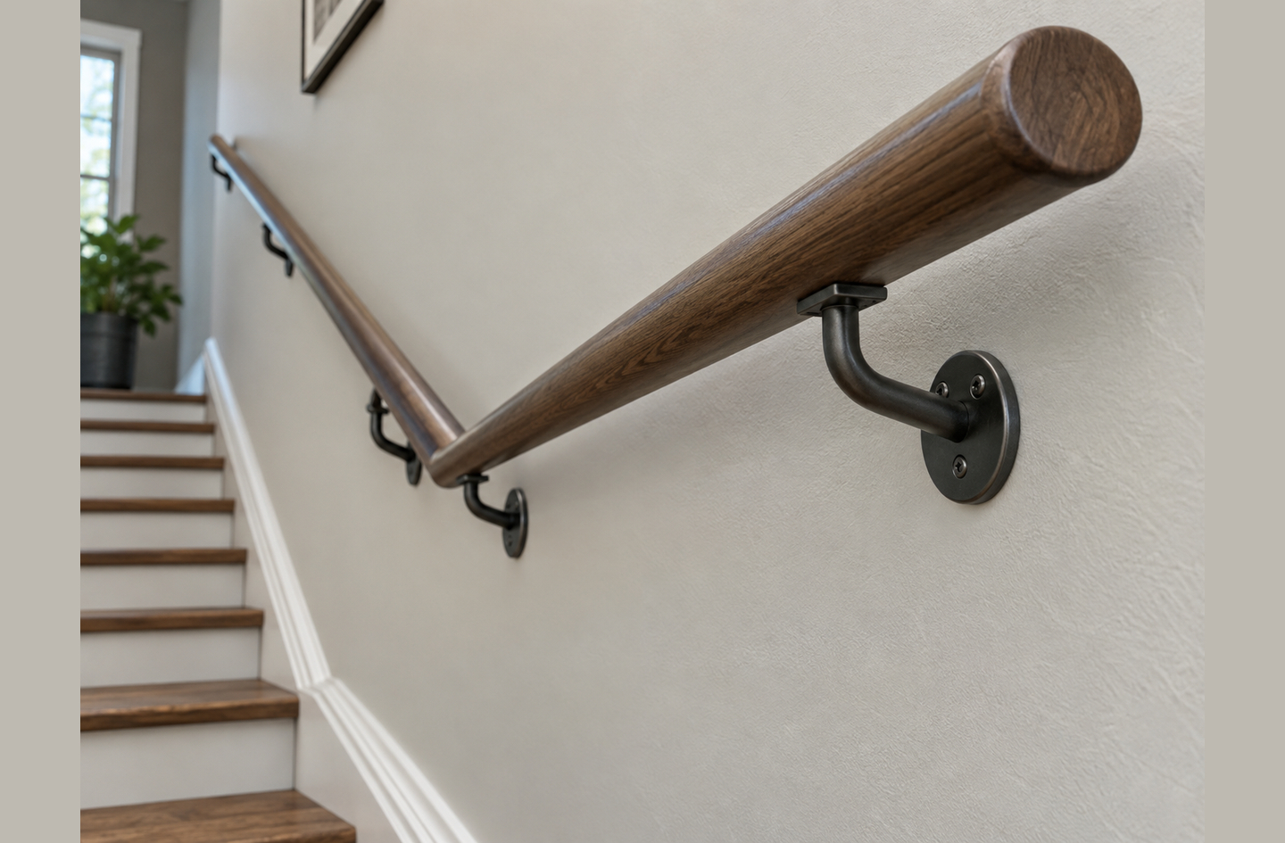 A dark-stained wooden handrail mounted along a staircase with industrial dark-metal brackets, a profile that pairs a graspable round section with a visible mounting pattern.