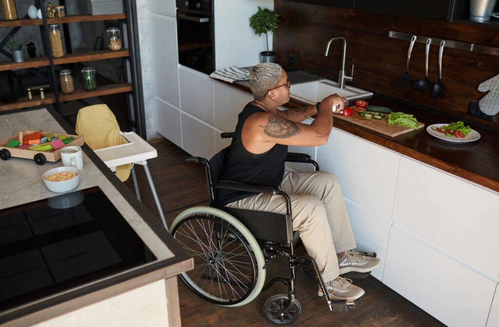 Accessible kitchen design in use: a person in a wheelchair cuts vegetables on a wooden board at a kitchen island