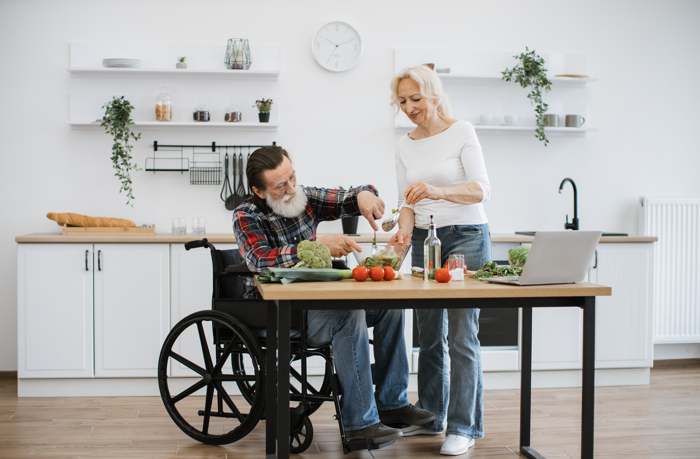 Senior man in a wheelchair and a woman preparing a salad together at an accessible kitchen table