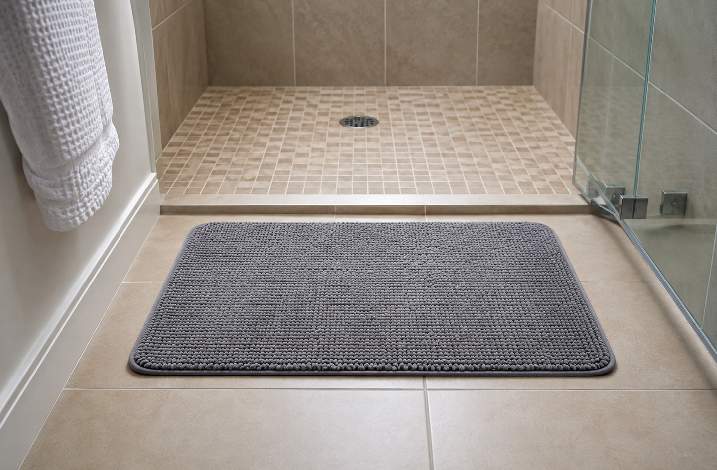 A grey textured slip-resistant mat lying on the tiled bathroom floor directly outside a walk-in shower, where wet feet first land.